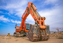 Bagger auf einer Baustelle unter blauem Himmel, mit einem großen Eimer zum Graben und Bewegen von Erde.