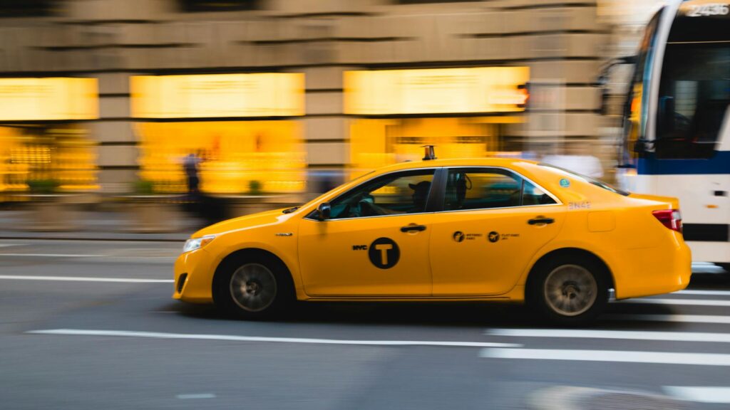 Ein gelbes New Yorker Taxi fährt schnell vorbei, während die Umgebung verschwommen ist.