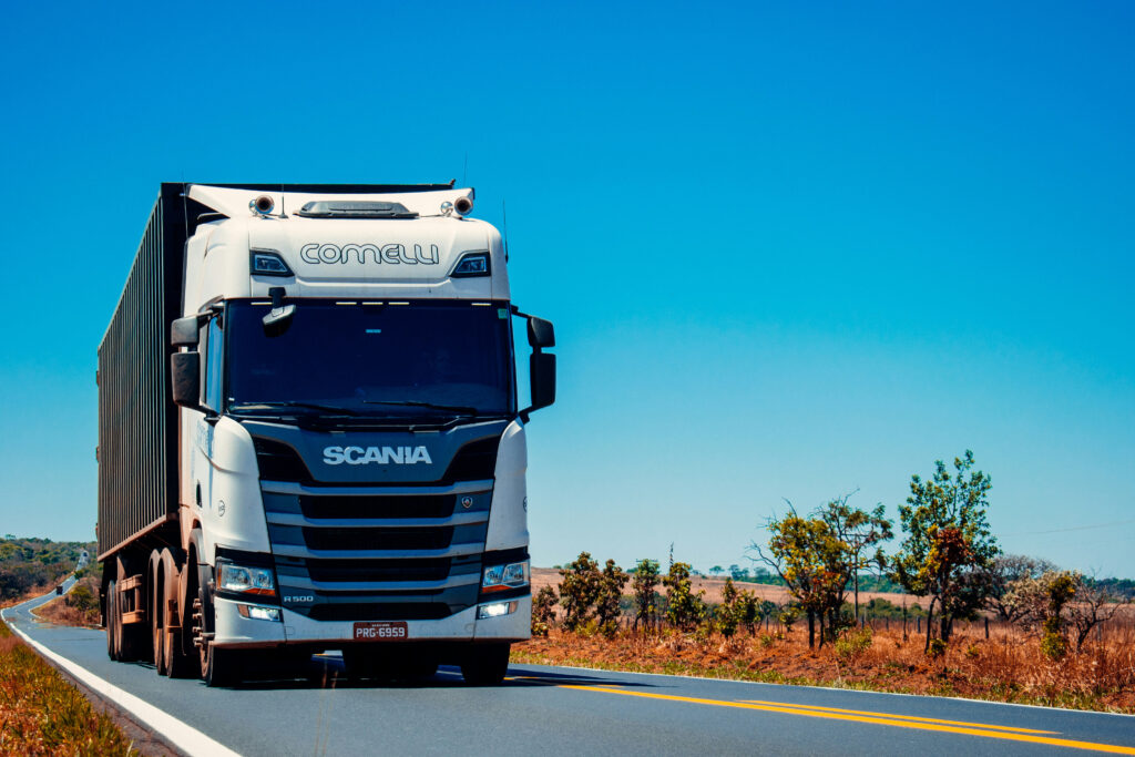 Ein Scania-Lkw fährt auf einer kurvenreichen Straße umgeben von lichtem Grün und blauem Himmel.