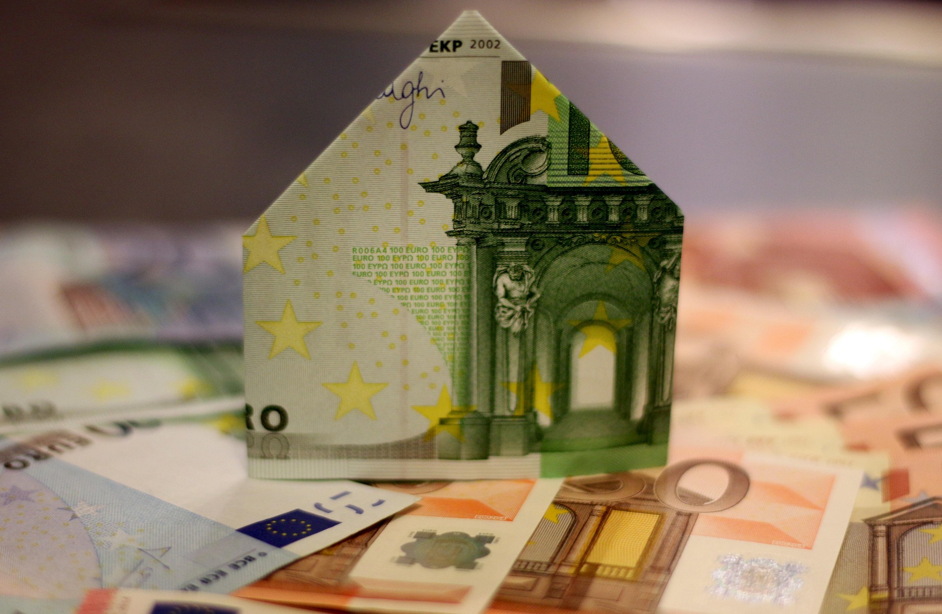 Ein Haus aus Geldscheinen steht auf weiteren Euro-Banknoten. Die Szene symbolisiert Finanz- oder Immobilienthemen.