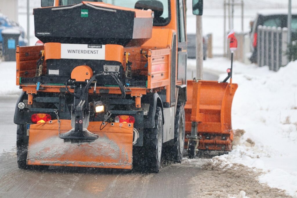Ein Winterdienstfahrzeug räumt schneebedeckte Straßen mit einem Schneepflug und streut Salz.