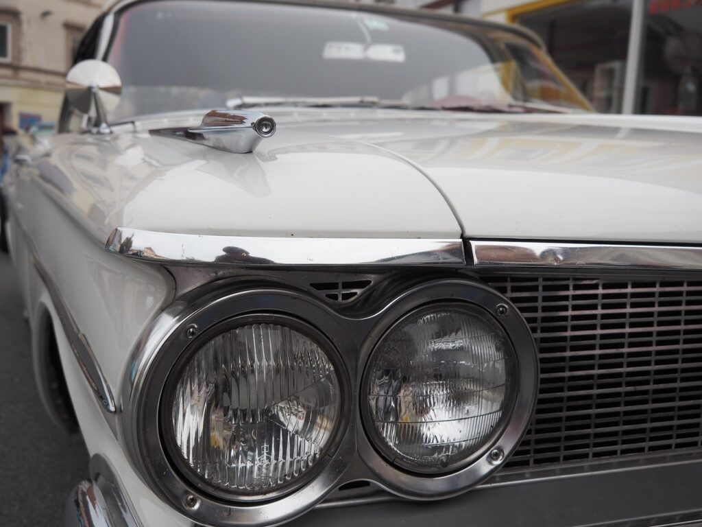 Nahaufnahme eines weißen Oldtimers mit verchromten Details und zwei runden Scheinwerfern.